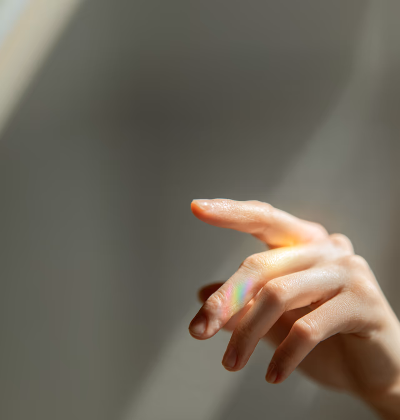 Close-up of a hand with fingers slightly bent and a small rainbow reflection on the skin.